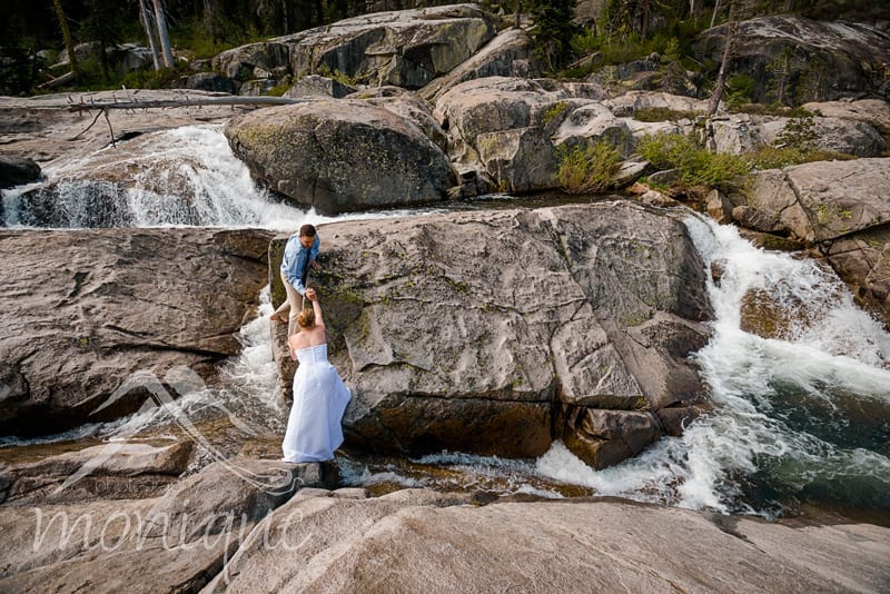bride and groom climb rocks in river