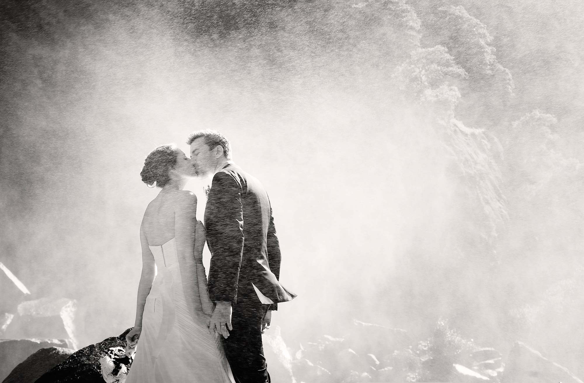Award-winning black and white photograph of a bride and groom kissing under Yosemite Falls during their Yosemite Valley wedding. Image by Photography by Monqiue, Lake Tahoe wedding photographer.