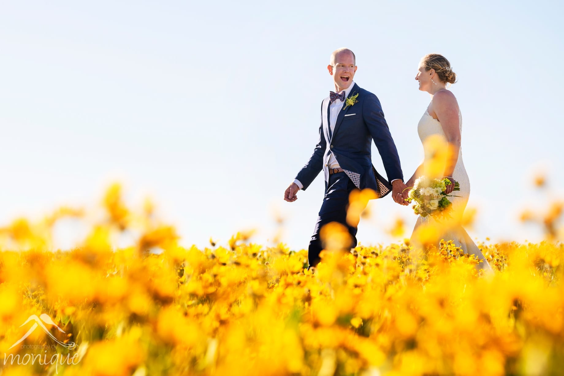 Squaw Valley High Camp wedding photography with the bride and groom walking through a filed of yellow wild flowers by Photography by Monique